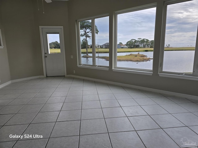 empty room with ceiling fan, a water view, and light tile patterned floors