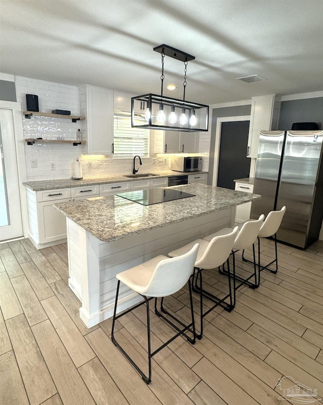 kitchen with visible vents, a sink, wood finish floors, stainless steel appliances, and backsplash