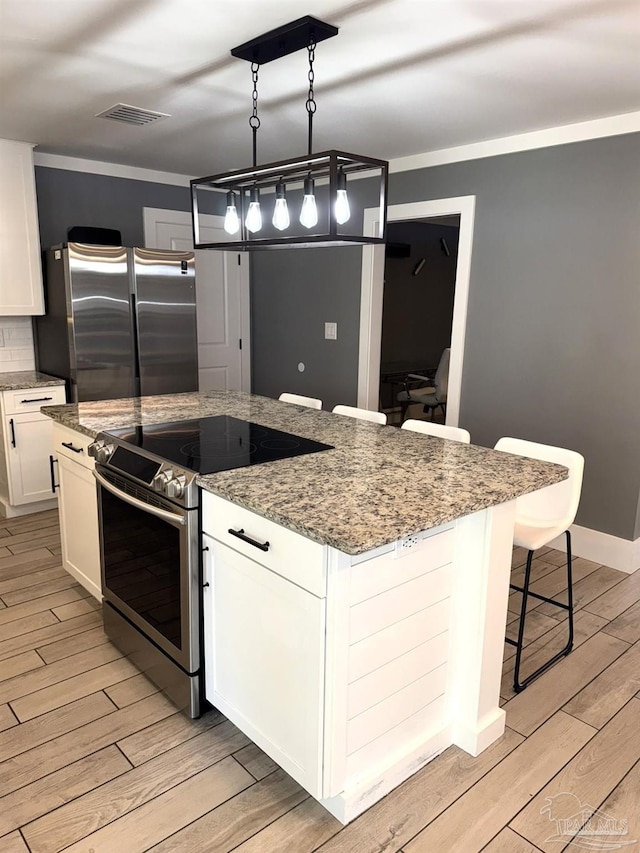 kitchen with white cabinets, light wood-type flooring, a kitchen island, and stainless steel appliances