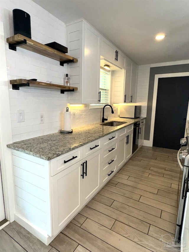 kitchen with a sink, backsplash, light wood-style flooring, and black dishwasher