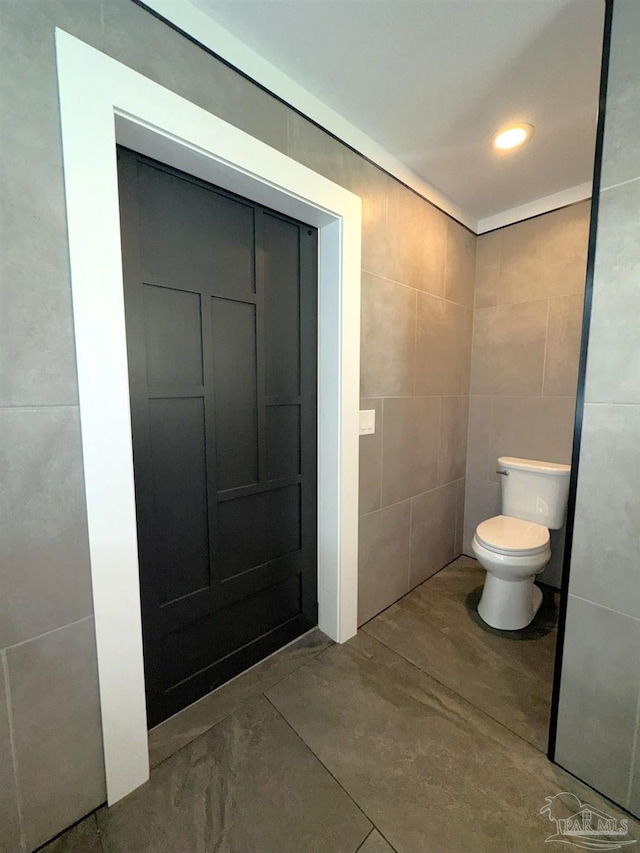 bathroom with toilet and tile walls