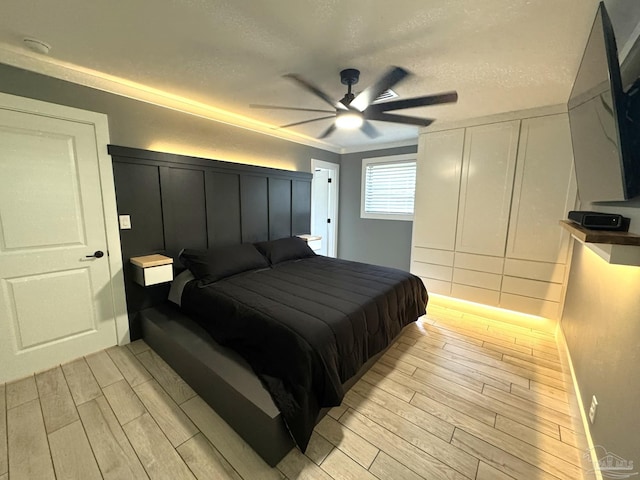 bedroom with a decorative wall, ceiling fan, a textured ceiling, and wood tiled floor