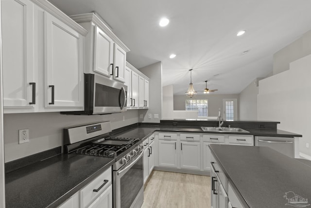 kitchen with dark countertops, appliances with stainless steel finishes, light wood-style floors, white cabinetry, and a sink