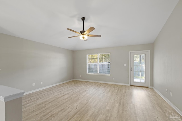 spare room featuring lofted ceiling, light wood-style floors, baseboards, and a wealth of natural light