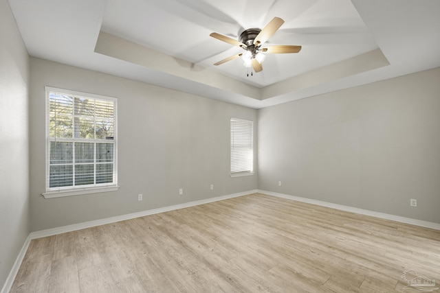 empty room with baseboards, a raised ceiling, and light wood-style flooring