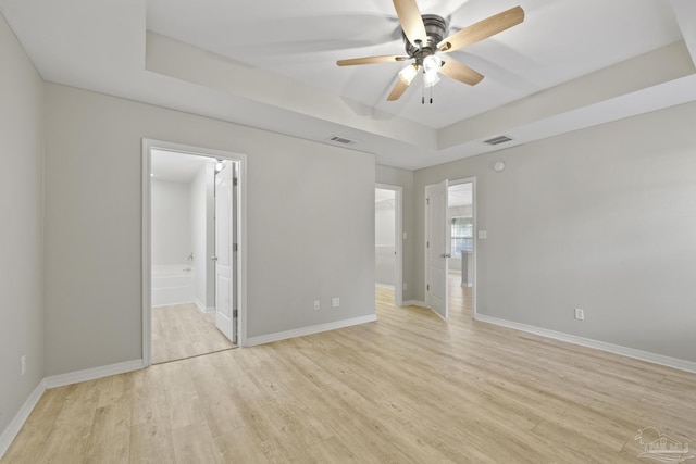 unfurnished bedroom with light wood-type flooring, a tray ceiling, baseboards, and visible vents