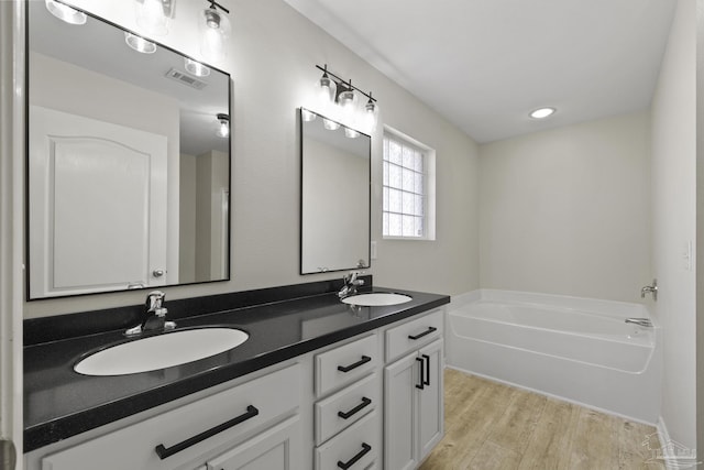 bathroom with a garden tub, wood finished floors, double vanity, and a sink