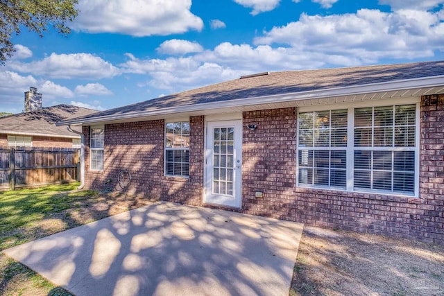 doorway to property featuring a patio, fence, brick siding, and roof with shingles