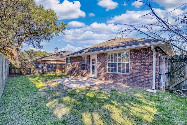 rear view of property with brick siding, a fenced backyard, a patio area, and a yard