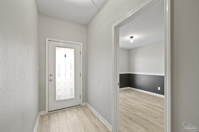 doorway with wood finished floors, baseboards, and a textured wall