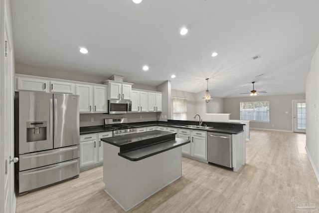 kitchen featuring a peninsula, a sink, stainless steel appliances, white cabinets, and dark countertops