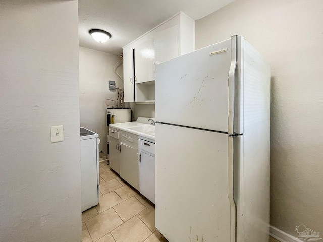 kitchen with light tile patterned floors, white cabinets, light countertops, freestanding refrigerator, and washer / dryer