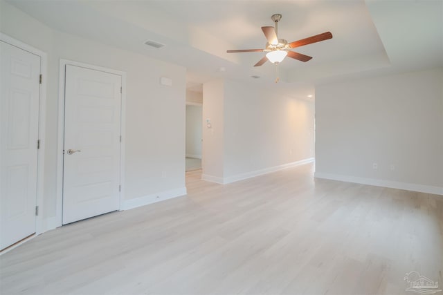 unfurnished room featuring a ceiling fan, baseboards, visible vents, light wood finished floors, and a tray ceiling