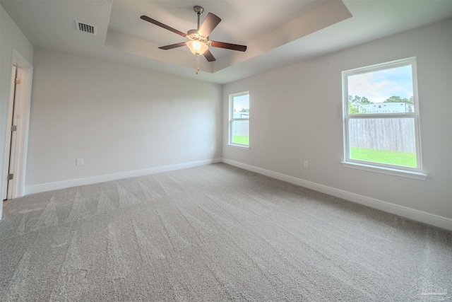 spare room with visible vents, carpet, baseboards, a raised ceiling, and a ceiling fan