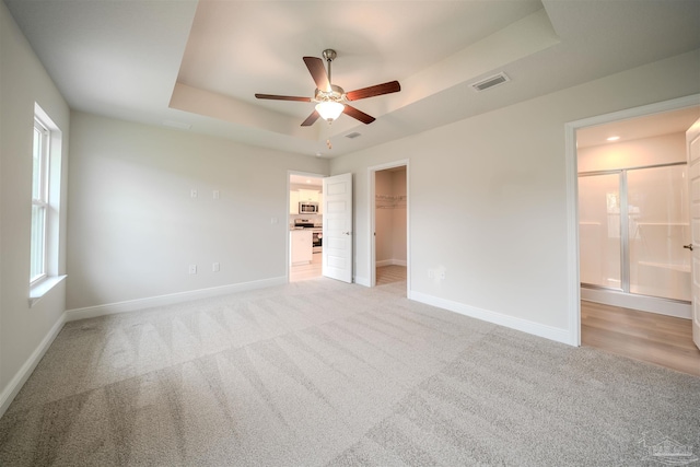 unfurnished bedroom with a spacious closet, visible vents, baseboards, light carpet, and a raised ceiling