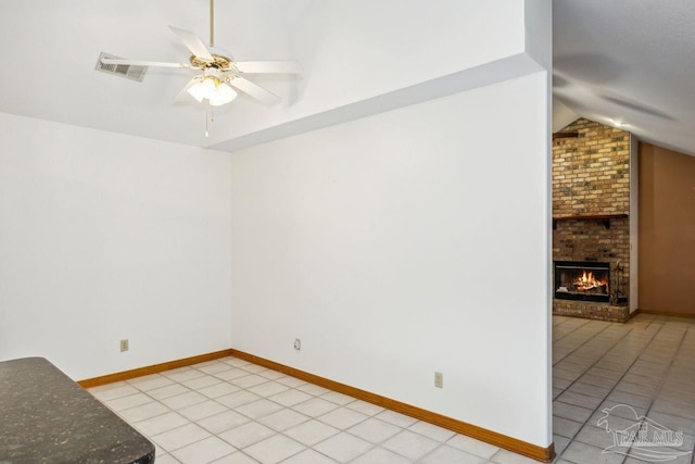 spare room with a fireplace, light tile patterned flooring, ceiling fan, and vaulted ceiling