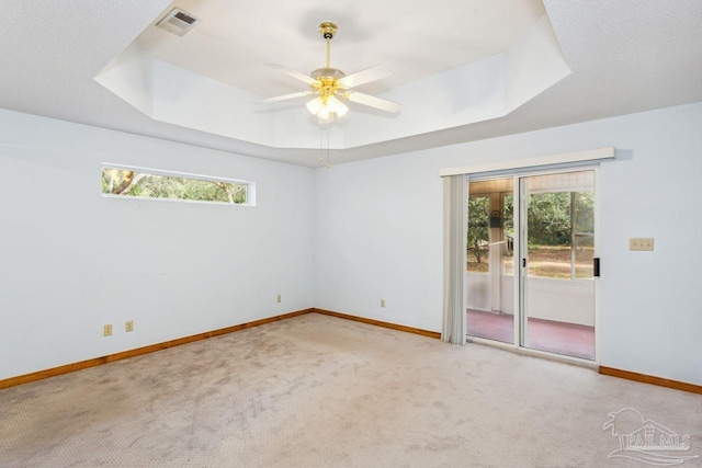 empty room with ceiling fan, light carpet, and a tray ceiling