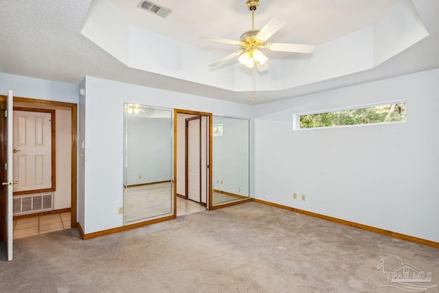 unfurnished bedroom with a tray ceiling, a textured ceiling, light colored carpet, and ceiling fan