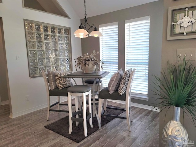 dining space featuring lofted ceiling, baseboards, a chandelier, and wood finished floors