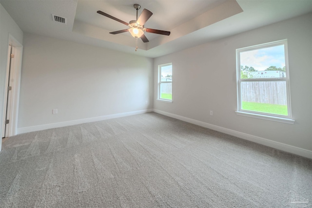 carpeted spare room with visible vents, ceiling fan, baseboards, and a tray ceiling