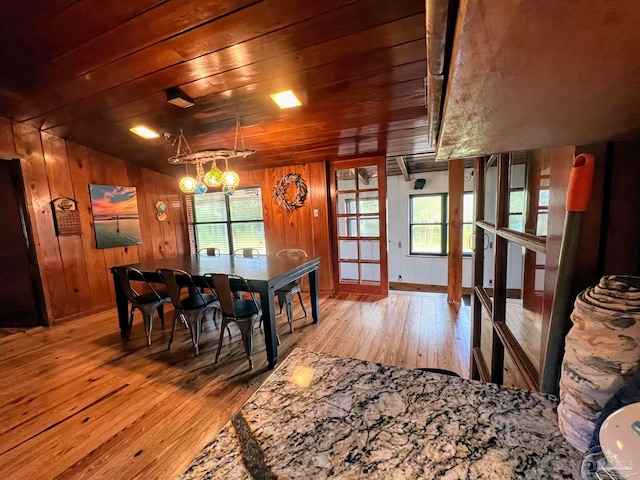 dining area with light hardwood / wood-style floors, vaulted ceiling, a notable chandelier, wooden walls, and wooden ceiling