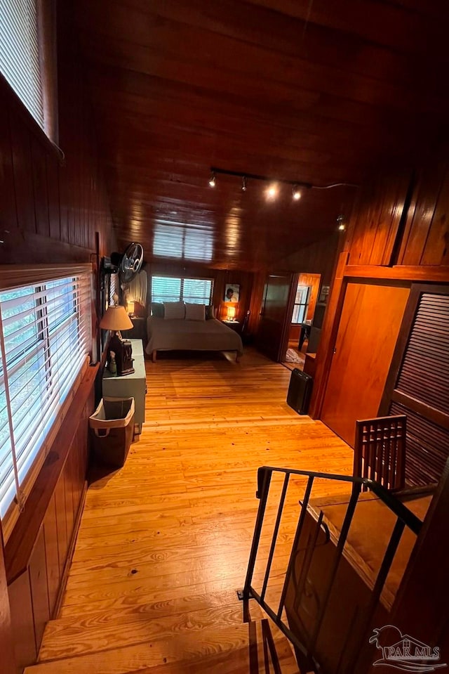 hall with light wood-type flooring, wooden walls, wood ceiling, and rail lighting