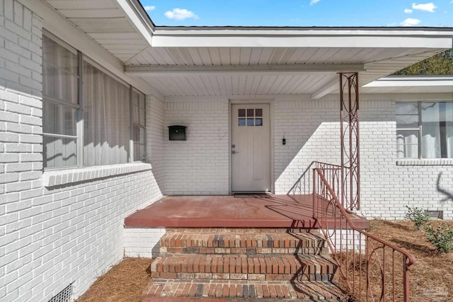 view of exterior entry featuring visible vents, brick siding, and crawl space