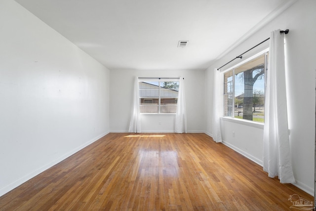 empty room with plenty of natural light, baseboards, and wood-type flooring