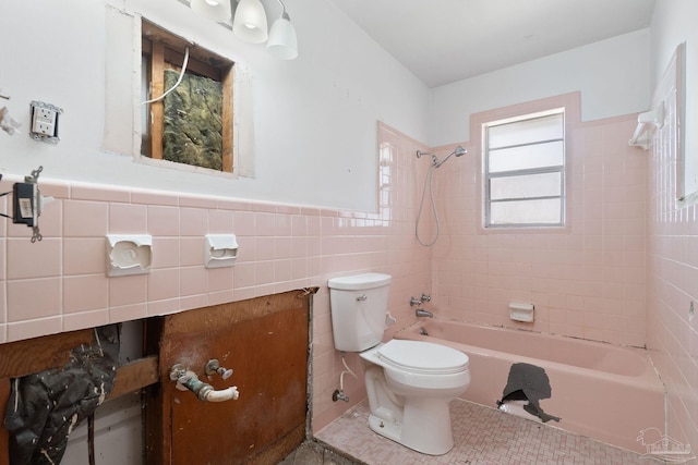 bathroom featuring a wainscoted wall, tile patterned flooring, tile walls, toilet, and shower / bathtub combination