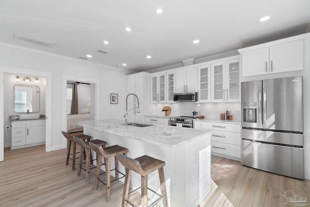 kitchen with a kitchen island with sink, a sink, appliances with stainless steel finishes, crown molding, and tasteful backsplash