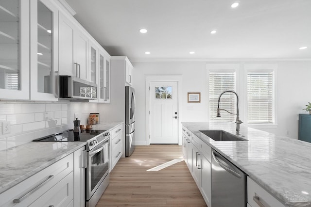 kitchen featuring backsplash, ornamental molding, white cabinets, stainless steel appliances, and a sink