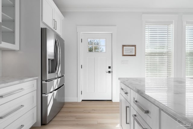 kitchen featuring light wood finished floors, glass insert cabinets, ornamental molding, white cabinets, and stainless steel fridge