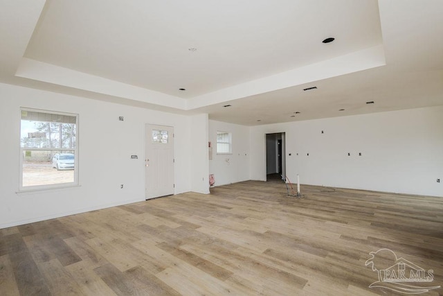 unfurnished living room featuring a tray ceiling, visible vents, a healthy amount of sunlight, and light wood-style flooring