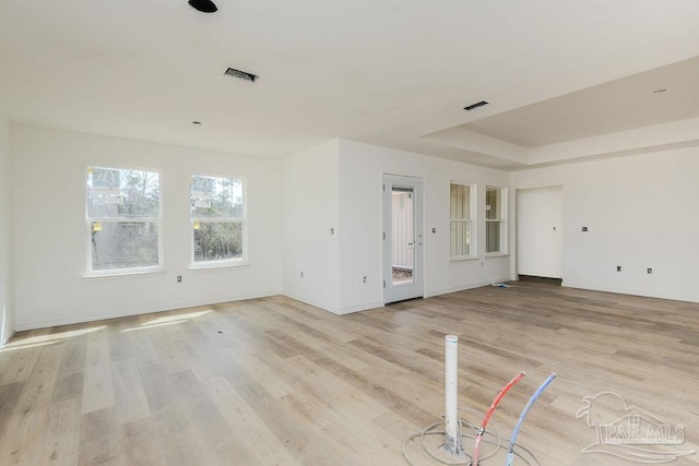 unfurnished living room with baseboards, light wood-style flooring, visible vents, and a tray ceiling