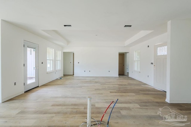 unfurnished living room with light wood-type flooring, visible vents, and a tray ceiling