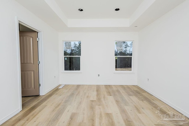 unfurnished room featuring a tray ceiling, light wood-type flooring, and baseboards