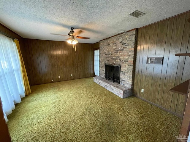 unfurnished living room featuring wood walls, ceiling fan, a textured ceiling, a brick fireplace, and carpet floors