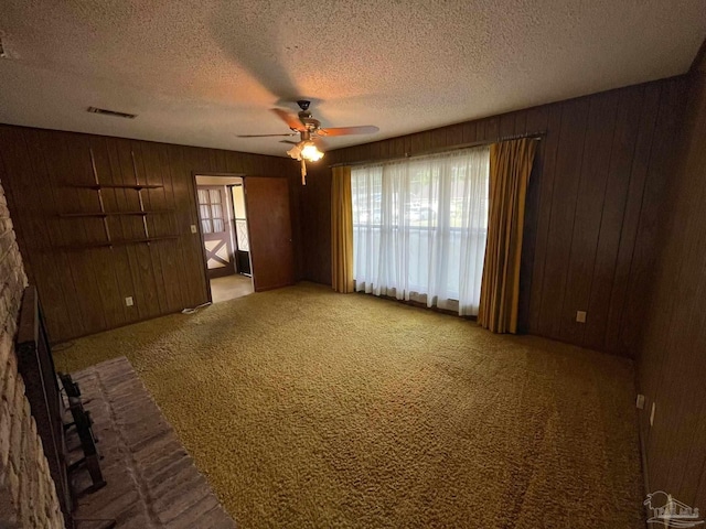 carpeted spare room featuring wood walls, a textured ceiling, and ceiling fan