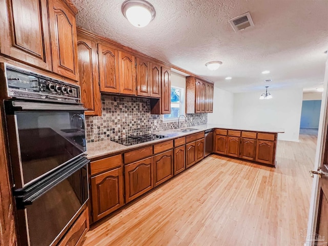 kitchen featuring brown cabinets, a peninsula, light wood-type flooring, black appliances, and a sink