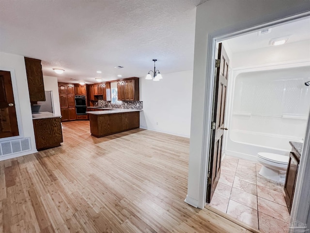 kitchen featuring a peninsula, light wood-style floors, visible vents, and decorative backsplash