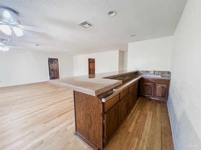 kitchen featuring visible vents, open floor plan, a textured ceiling, light wood-type flooring, and a peninsula