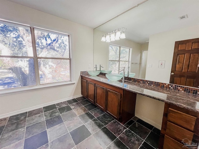 bathroom featuring a sink, visible vents, baseboards, backsplash, and double vanity