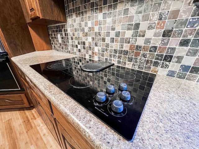 kitchen featuring tasteful backsplash, black electric stovetop, brown cabinets, and light wood finished floors