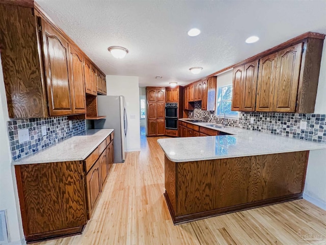 kitchen featuring decorative backsplash, freestanding refrigerator, a peninsula, light wood-type flooring, and a sink