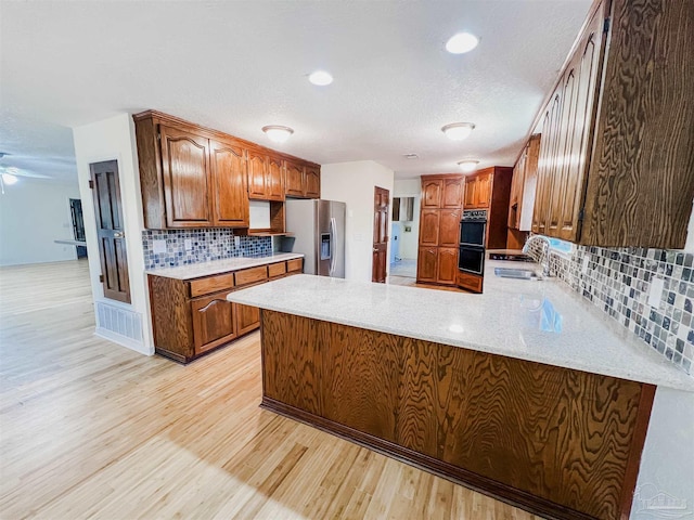 kitchen with light wood-style flooring, a peninsula, a sink, stainless steel refrigerator with ice dispenser, and decorative backsplash