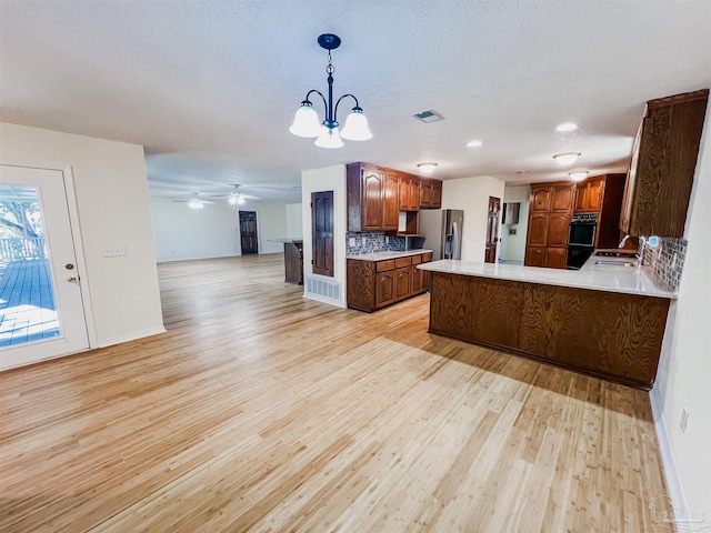 kitchen featuring light wood-style flooring, open floor plan, a peninsula, light countertops, and stainless steel refrigerator with ice dispenser