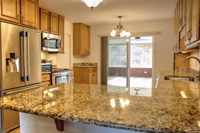 kitchen with sink, light stone counters, appliances with stainless steel finishes, kitchen peninsula, and pendant lighting