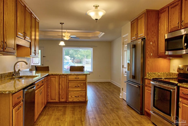 kitchen with appliances with stainless steel finishes, kitchen peninsula, sink, light stone counters, and a tray ceiling