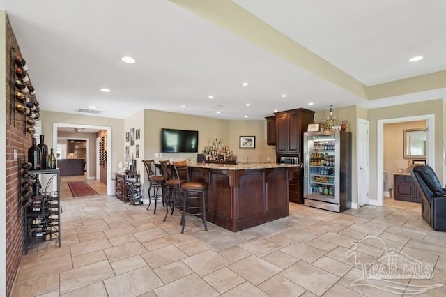 kitchen with dark brown cabinets, light tile patterned floors, a kitchen island, light stone countertops, and a kitchen bar