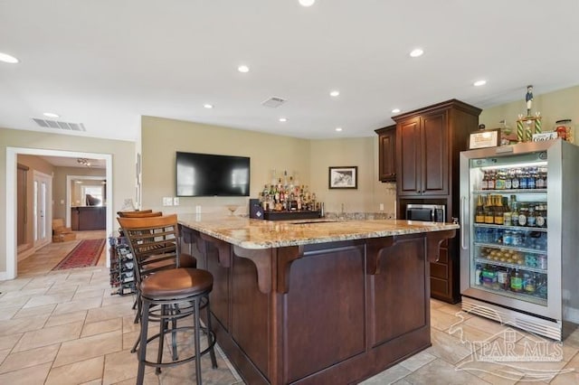 bar featuring light tile patterned flooring, fridge, dark brown cabinets, and light stone countertops